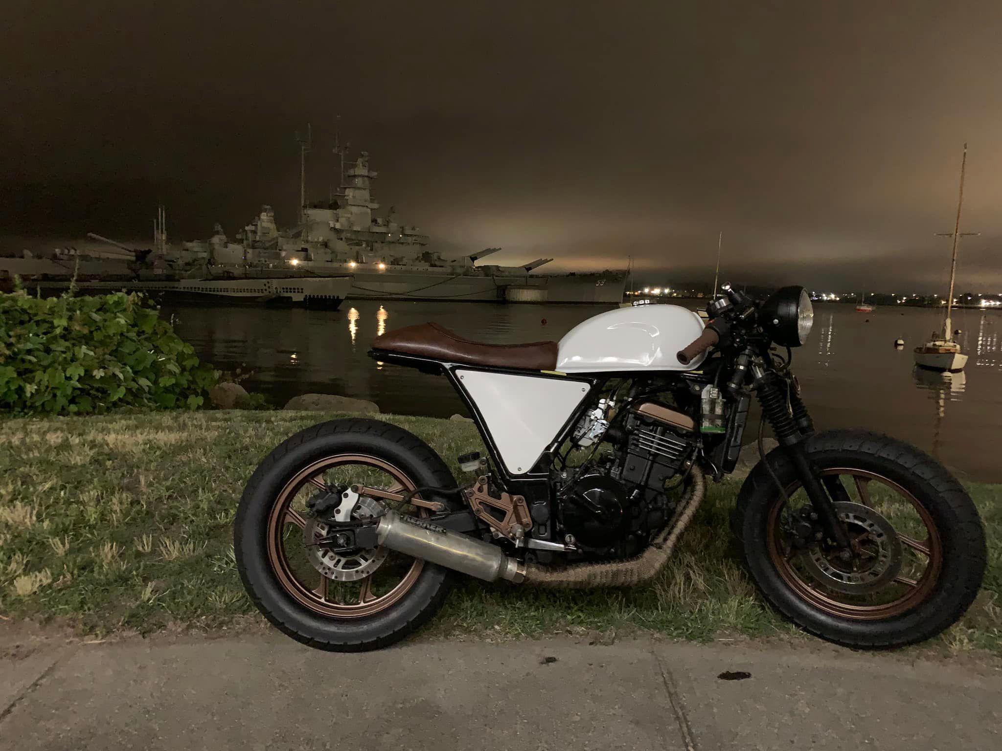 Cafe racer with battleship backdrop at night